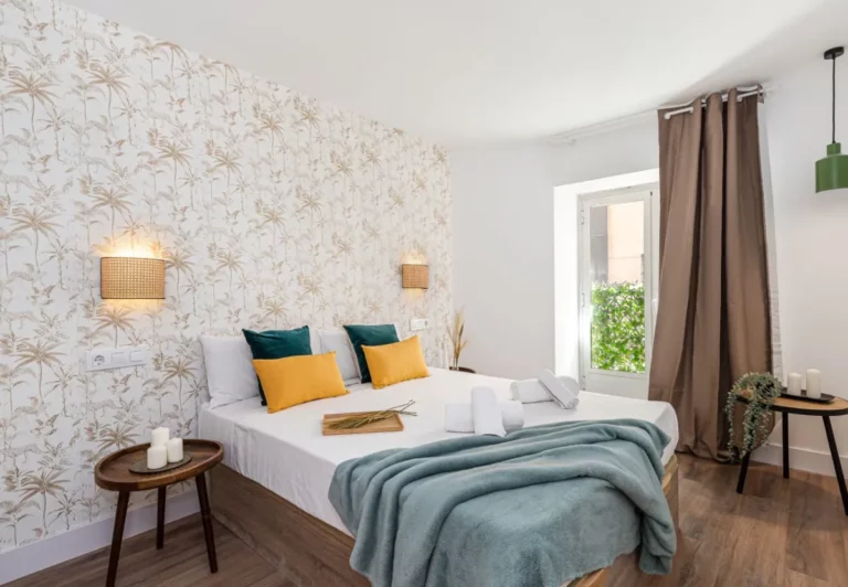 Dormitorio con papel de hojas y cojines verdes en el apartamento Queen's Chueca II, Madrid