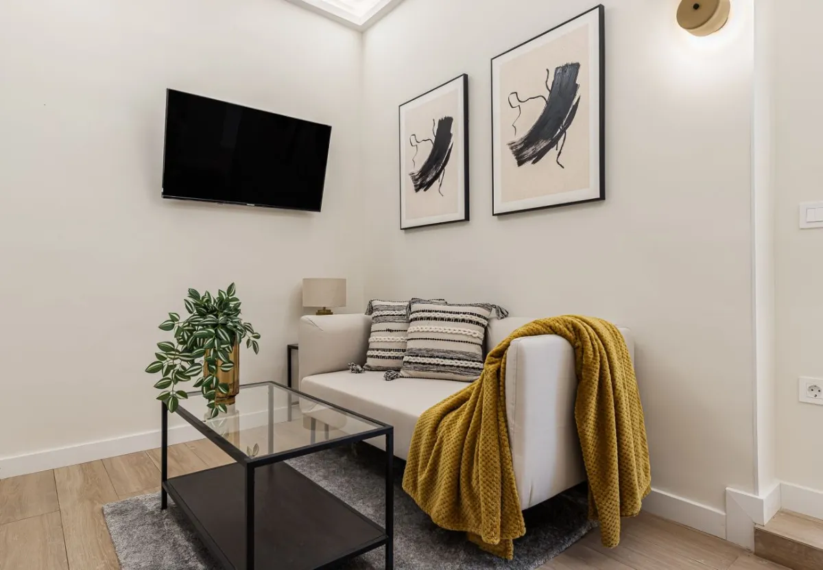 Salón con sofá y manta mostaza en el apartamento Queen's Chueca IV, Madrid