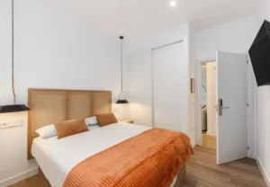 Cama de matrimonio con colcha teja en la habitación Queen's Bernabéu I, coliving en Chamartín, Madrid