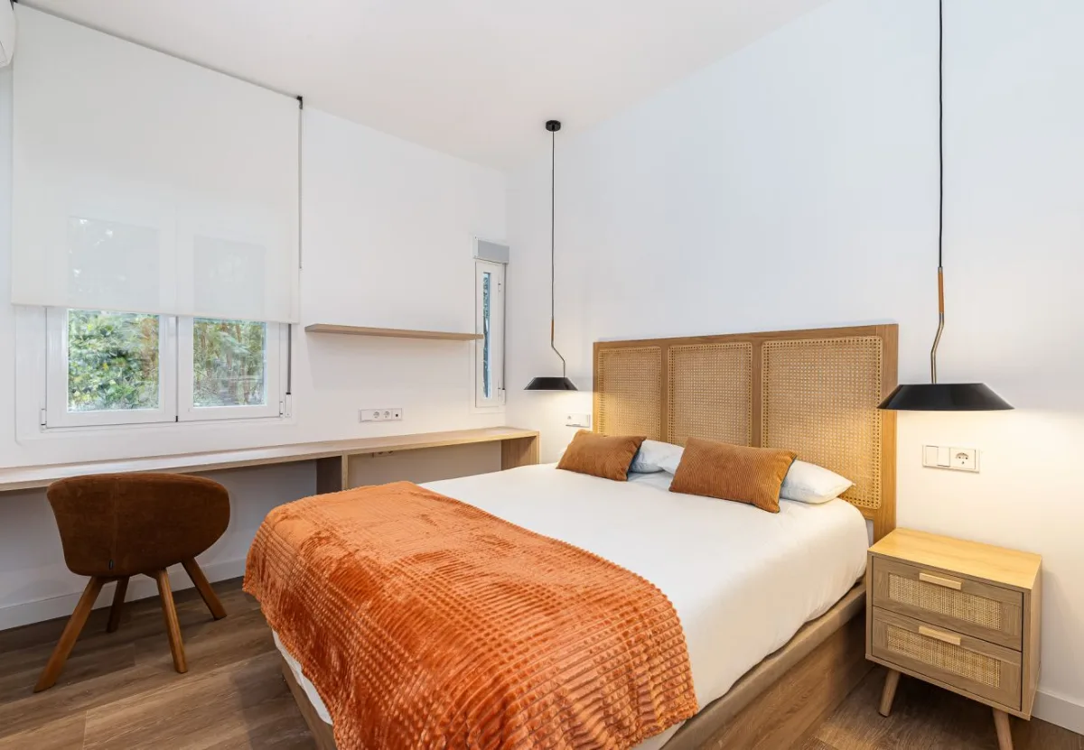 Dormitorio con cabecero de rejilla y escritorio bajo la ventana en la habitación Queen's Bernabéu I, coliving en Chamartín, Madrid