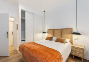 Cama con colcha teja y cojines terracota en la habitación Queen's Bernabéu II, coliving en Chamartín, Madrid