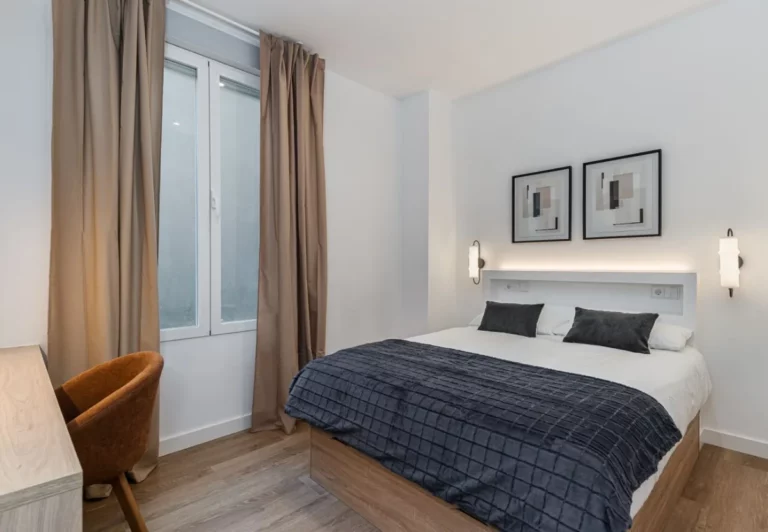 Dormitorio con colcha azul marino y dos cuadros en la habitación Queen's Bernabéu IV, coliving en Chamartín, Madrid