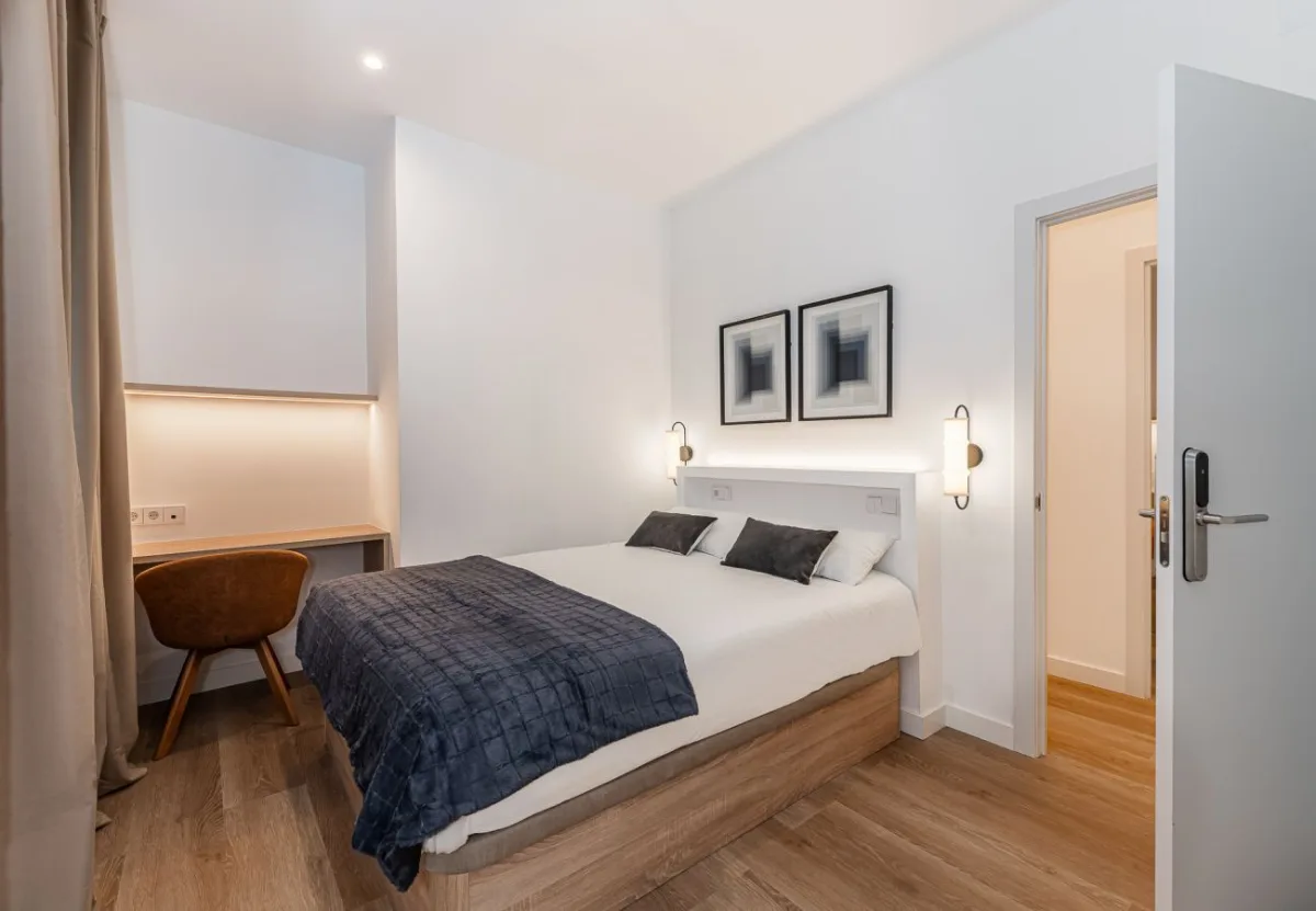 Dormitorio con colcha azul marino y escritorio en la habitación Queen's Bernabéu V, coliving en Chamartín, Madrid