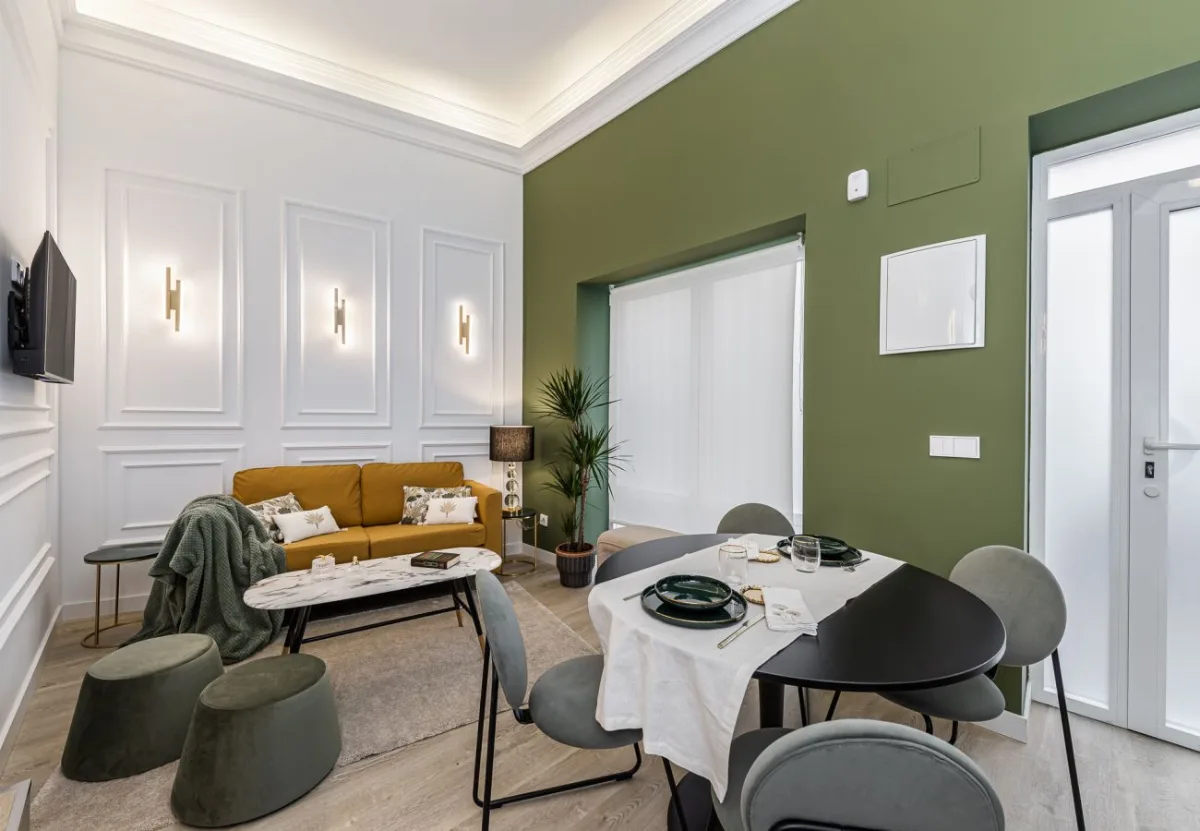 Salón con sofá mostaza y pared verde en el apartamento Queen's Chamberí II, Madrid