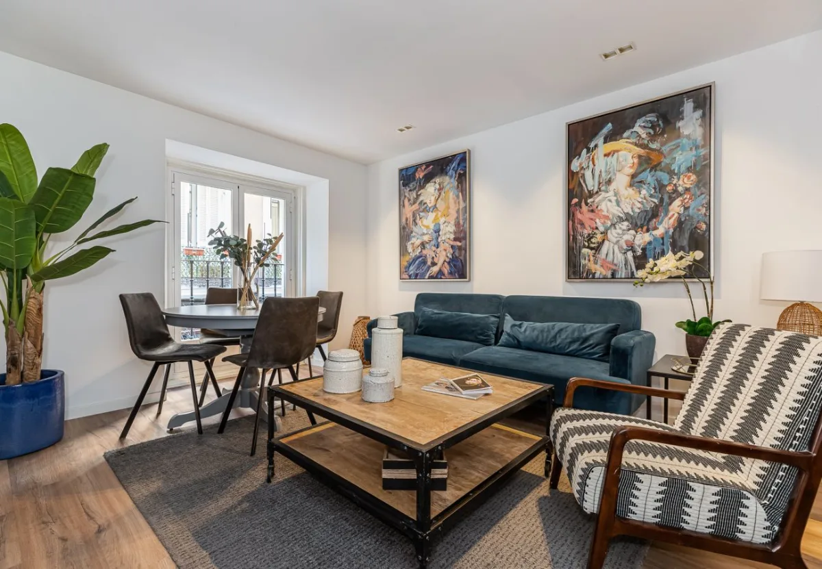 Salón con sofá azul y comedor junto a la ventana en el apartamento Queen's Chueca I, Madrid