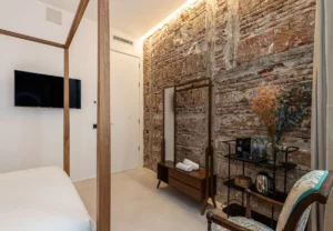 Pared de ladrillo visto y madera antigua en la habitación Queen's House Chueca I, hotel boutique en Chueca, Madrid