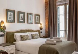 Cama de matrimonio junto a las ventanas balconeras en la habitación Queen's House Chueca III, hotel boutique en Chueca, Madrid