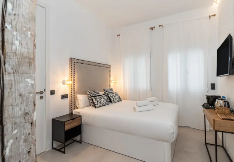 Dormitorio con paredes encaladas y cabecero con tachuelas en la habitación Queen's House Chueca VII, hotel boutique en Chueca, Madrid