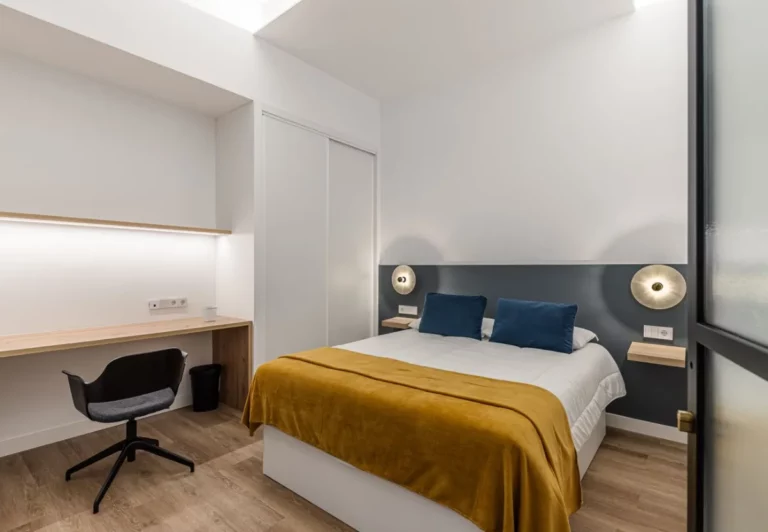 Dormitorio con colcha mostaza y escritorio en la habitación Queen's Olavide II, coliving en Chamberí, Madrid
