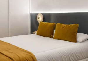 Cama con cojines mostaza en la habitación Queen's Olavide III, coliving en Chamberí, Madrid