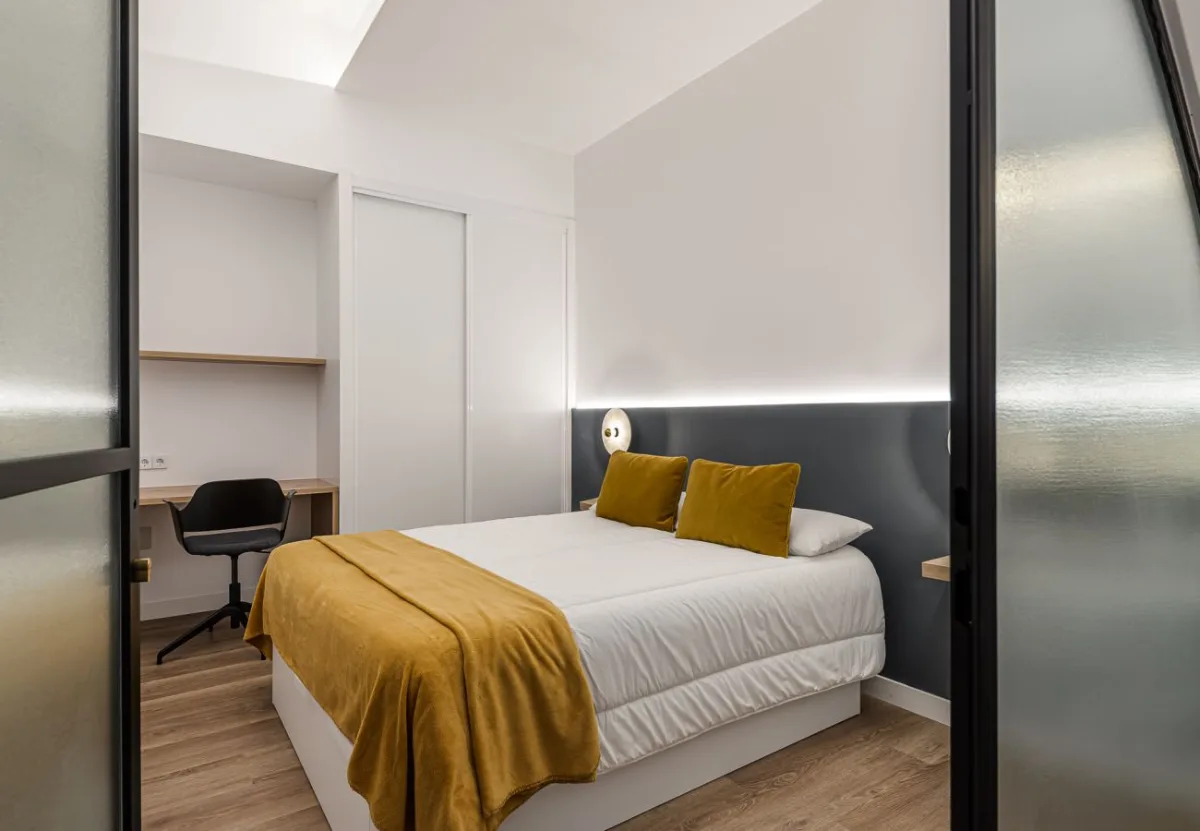 Dormitorio con colcha mostaza y escritorio en la habitación Queen's Olavide III, coliving en Chamberí, Madrid