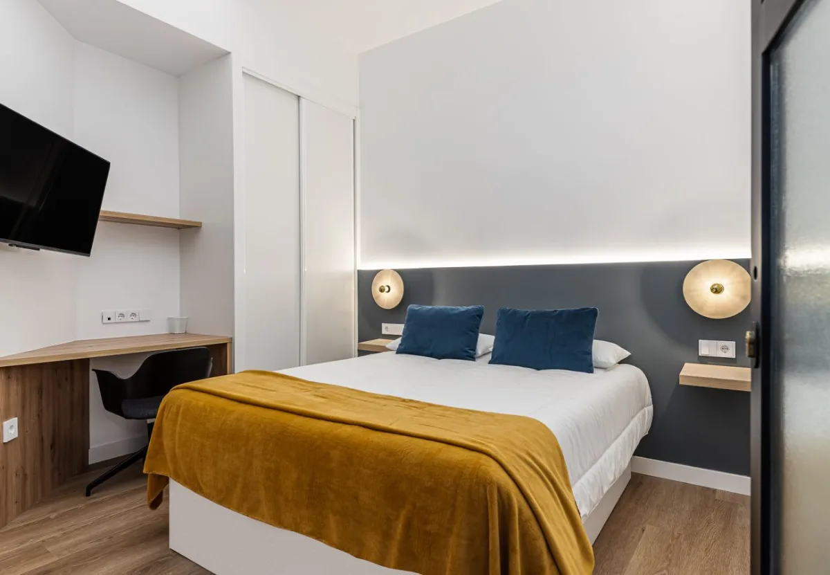 Dormitorio con cojines azul petróleo y escritorio en la habitación Queen's Olavide IV, coliving en Chamberí, Madrid