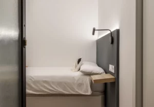 Cama individual con cabecero gris en la habitación Queen's Olavide V, coliving en Chamberí, Madrid