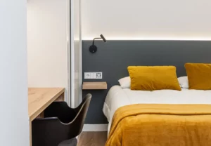 Cama con cojines mostaza en la habitación Queen's Olavide VI, coliving en Chamberí, Madrid