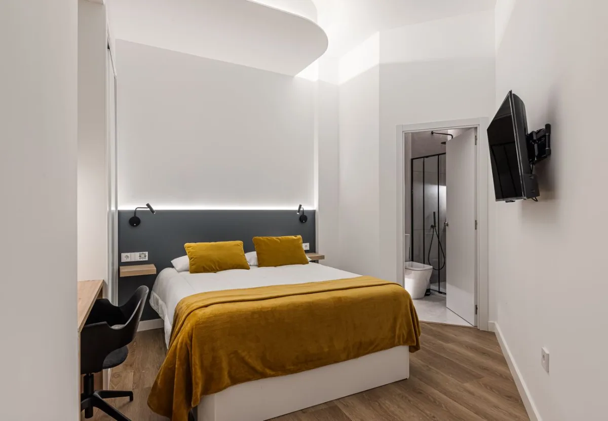 Dormitorio con colcha mostaza y escritorio en la habitación Queen's Olavide VI, coliving en Chamberí, Madrid