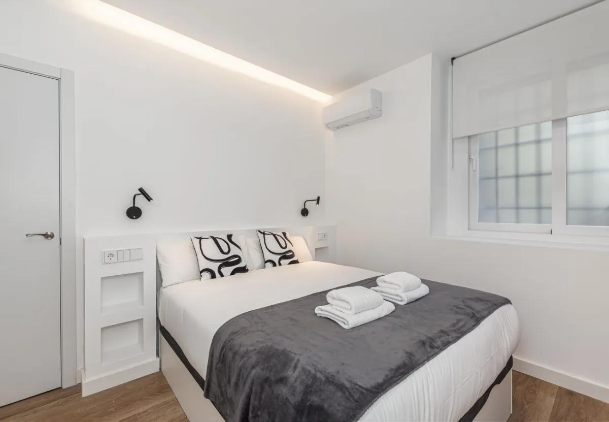Cama de matrimonio con cojines estampados y manta gris, Queen's Plaza España I, coliving en Argüelles, Madrid
