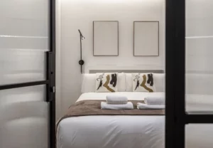 Cama con cojines estampados y manta marrón, Queen's Plaza España II, coliving en Argüelles, Madrid