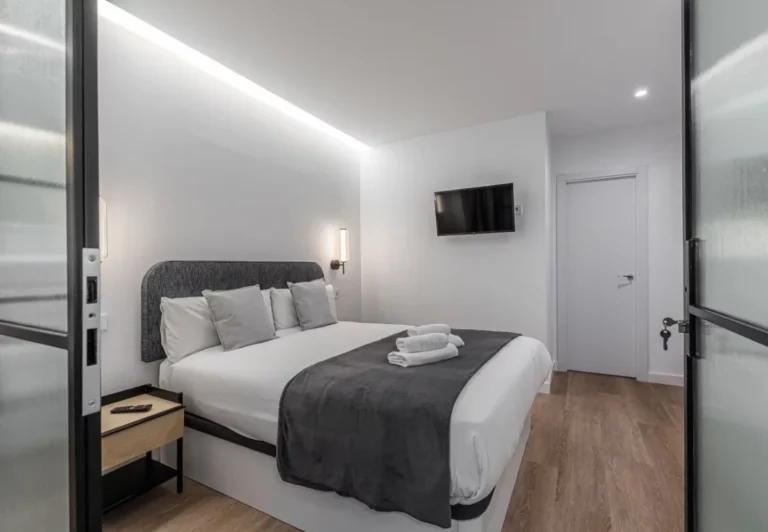 Cama de matrimonio con cabecero tapizado gris, Queen's Plaza España III, coliving en Argüelles, Madrid