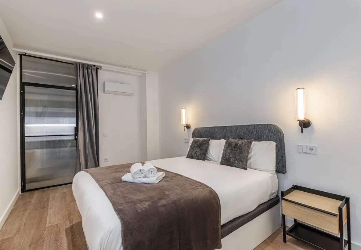 Cama de matrimonio con cabecero tapizado y mesitas de madera, Queen's Plaza España IV, coliving en Argüelles, Madrid