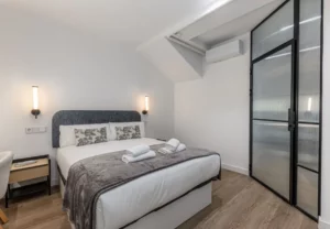 Cama con cojines estampados y puerta de cristal y acero, Queen's Plaza España V, coliving en Argüelles, Madrid