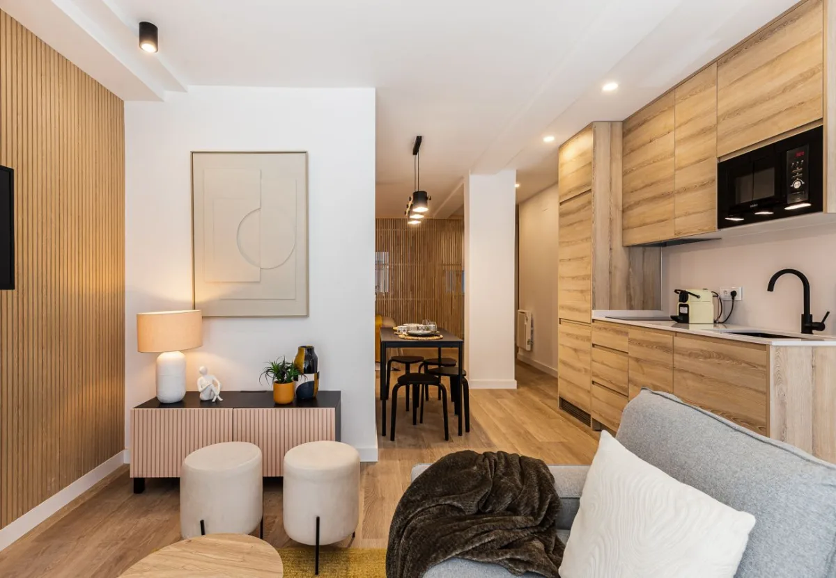 Salón con cocina abierta en madera clara en el apartamento Queen's Salamanca I, Madrid